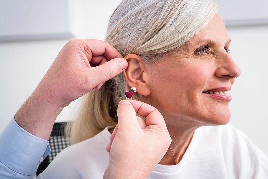 Eine ältere Frau bekommt von einem Hörakustiker ein modernes Hörgerät ins Ohr eingesetzt.